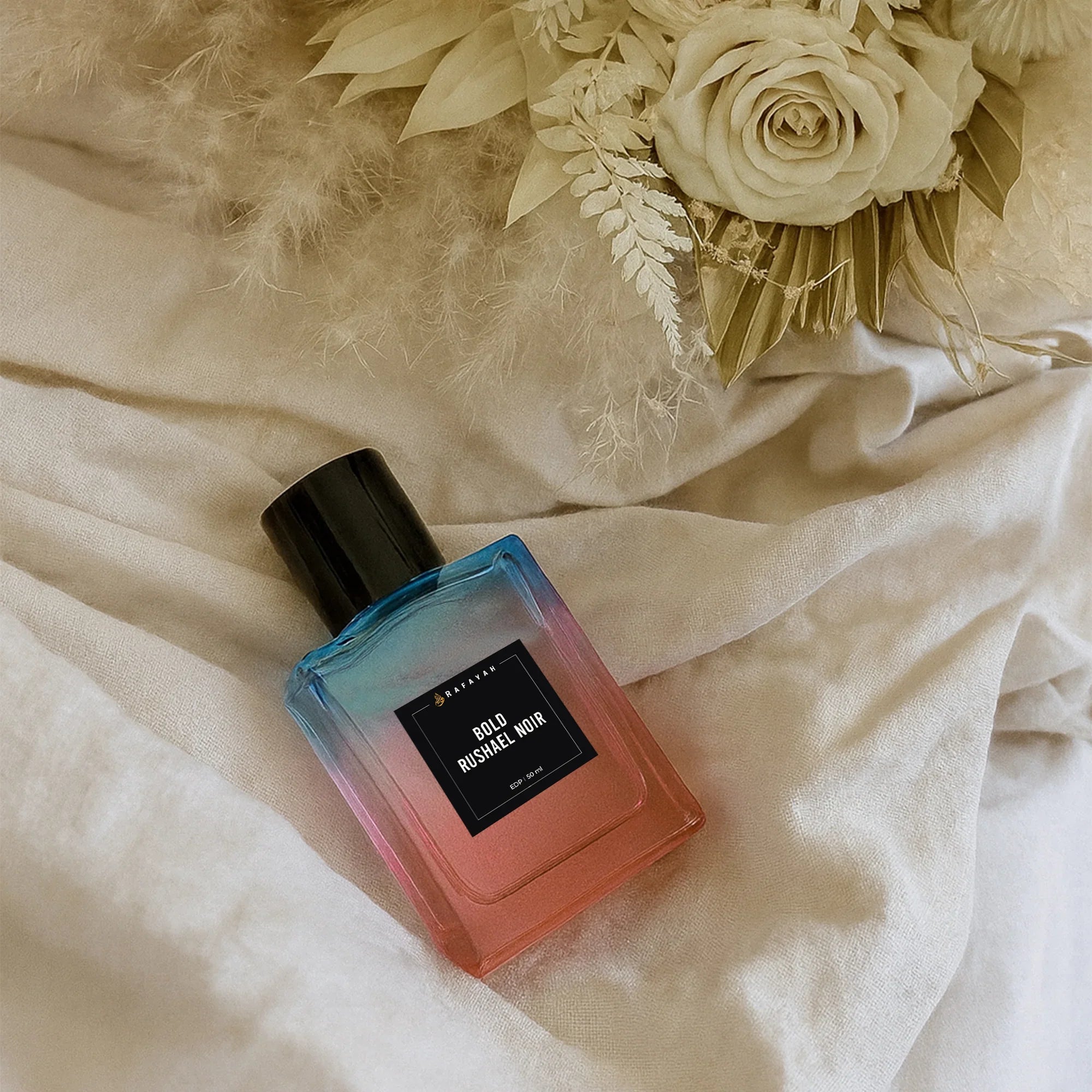 Bold Rushael Noir perfume bottle on soft beige fabric with white dried flowers
